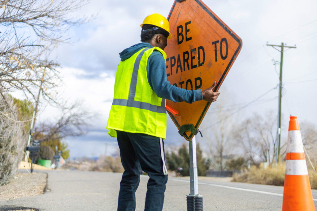 Man wearing safety gear moving a safety sign into place on a road